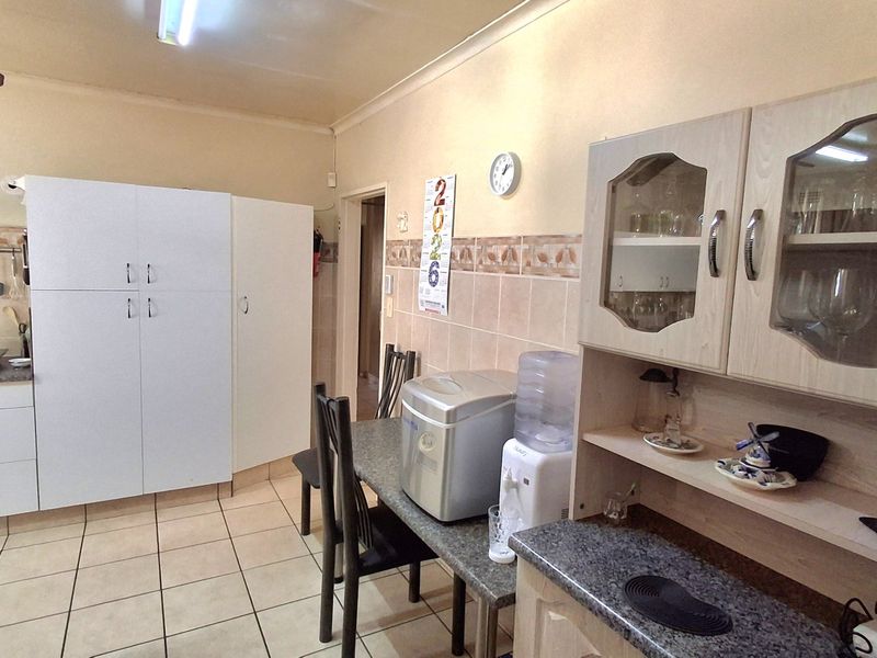A functional kitchen featuring tiled flooring, a tiled backsplash, and a combination of white and wood-tone built-in cabinetry with glass-fronted display units.