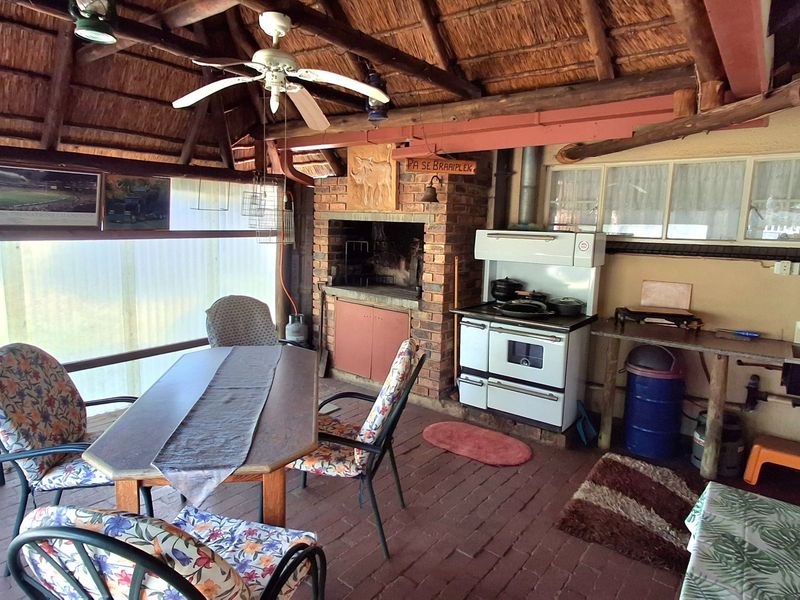 Covered outdoor patio featuring a thatched roof, built-in brick braai, and basic kitchen prep area with sink and stove.