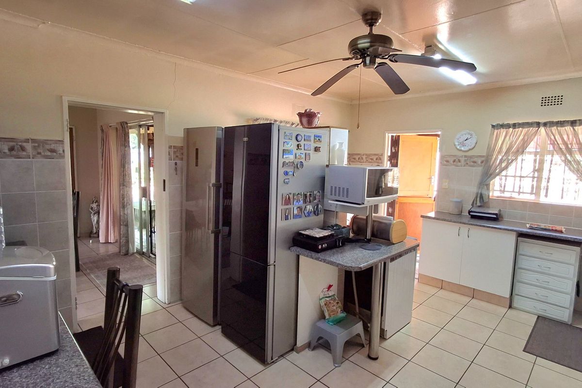 A functional kitchen featuring tiled flooring, built-in cabinetry, laminate countertops, and a ceiling fan, with visible wall plaster cracks requiring maintenance.