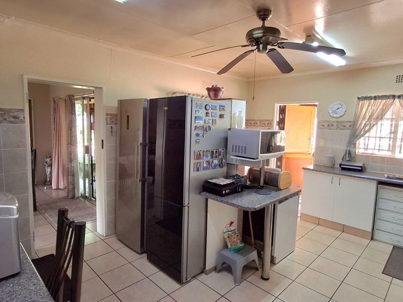 A functional kitchen featuring tiled flooring, built-in cabinetry, laminate countertops, and a ceiling fan, with visible wall plaster cracks requiring maintenance.