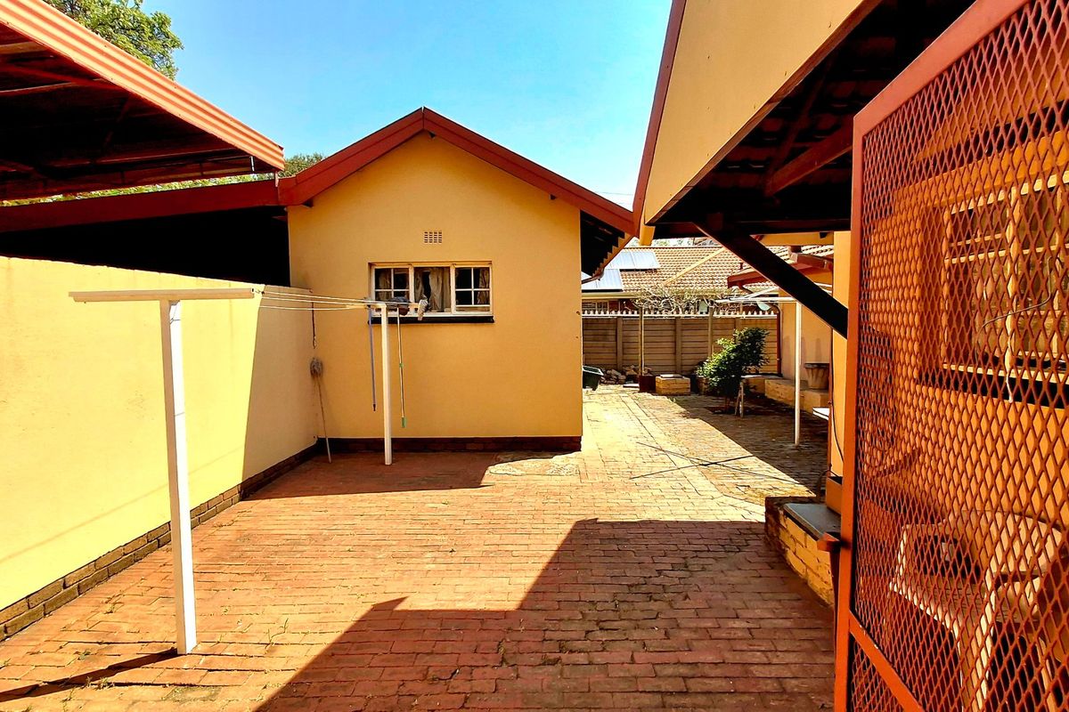 A paved rear courtyard area featuring a covered patio section, enclosed by boundary walls and a secure metal gate.