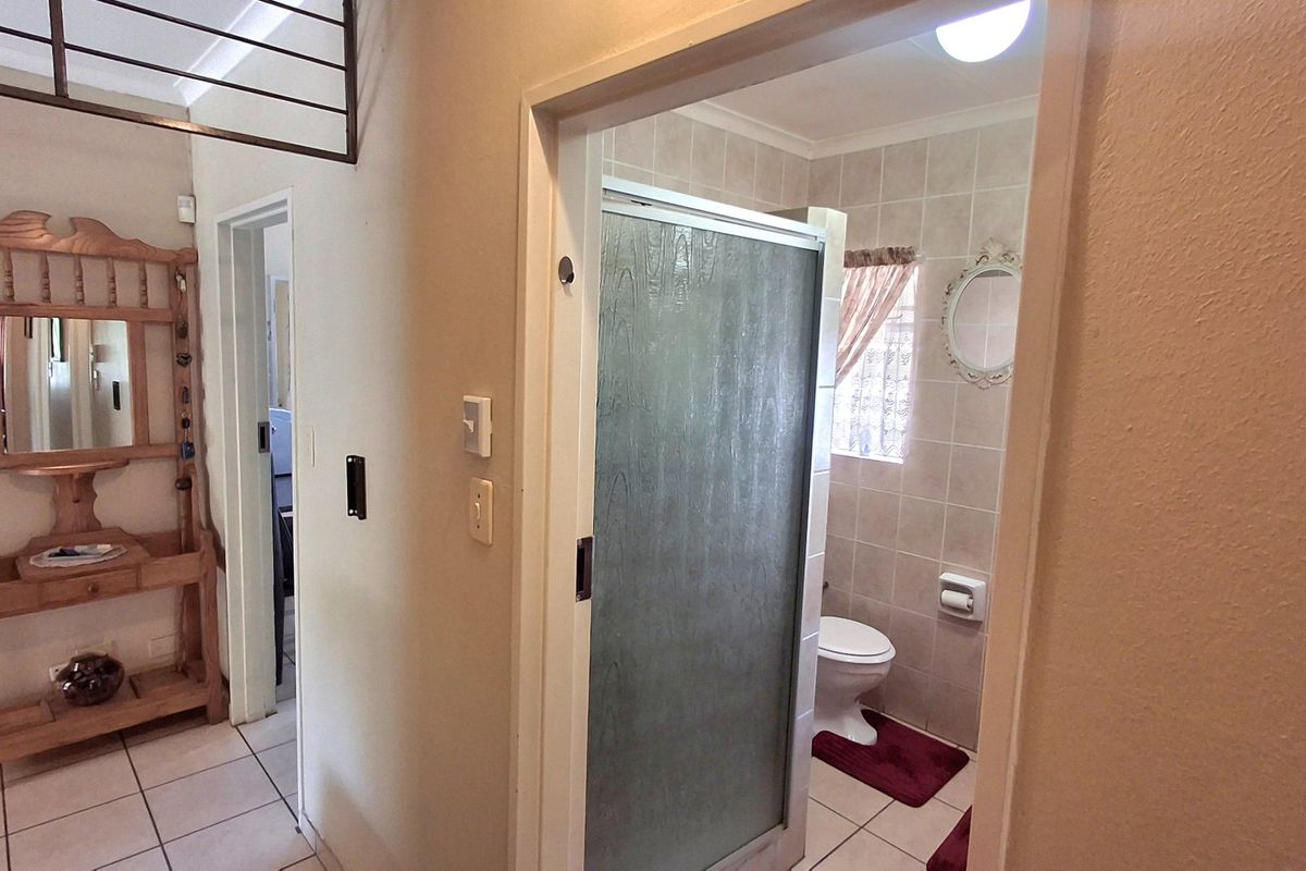 A functional bathroom featuring a shower enclosure, tiled walls, and tiled flooring, accessible from a hallway area.