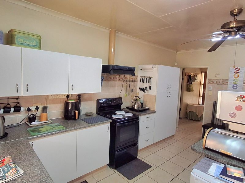 A functional kitchen featuring white cabinetry, laminate countertops, a tiled backsplash, and a freestanding stove with an extractor fan.