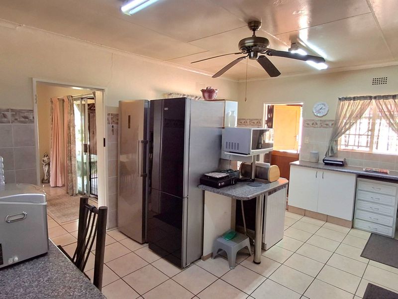 A functional kitchen featuring tiled flooring, built-in cabinetry with laminate countertops, and a ceiling fan, offering a practical layout with direct access to adjacent rooms.
