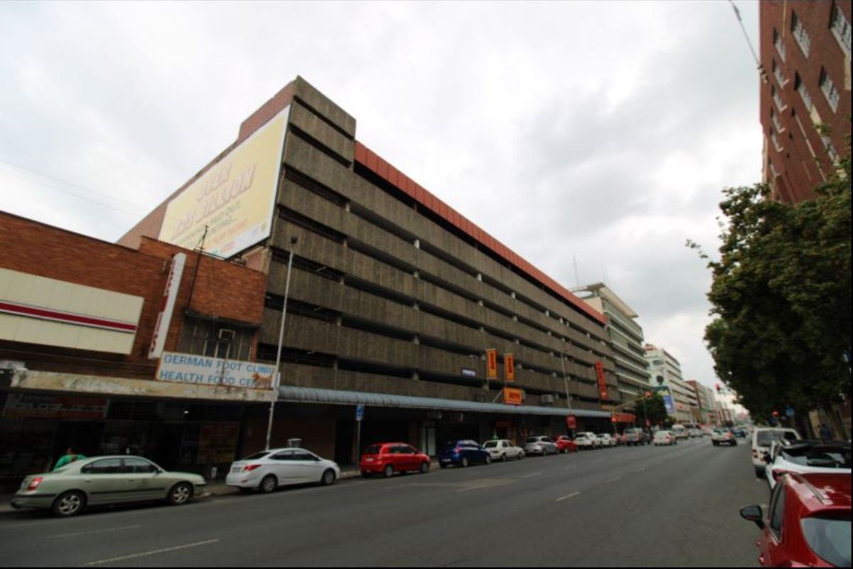 Street-level view of a multi-story commercial building featuring ground-floor retail spaces and an integrated parking structure with prominent exterior advertising.