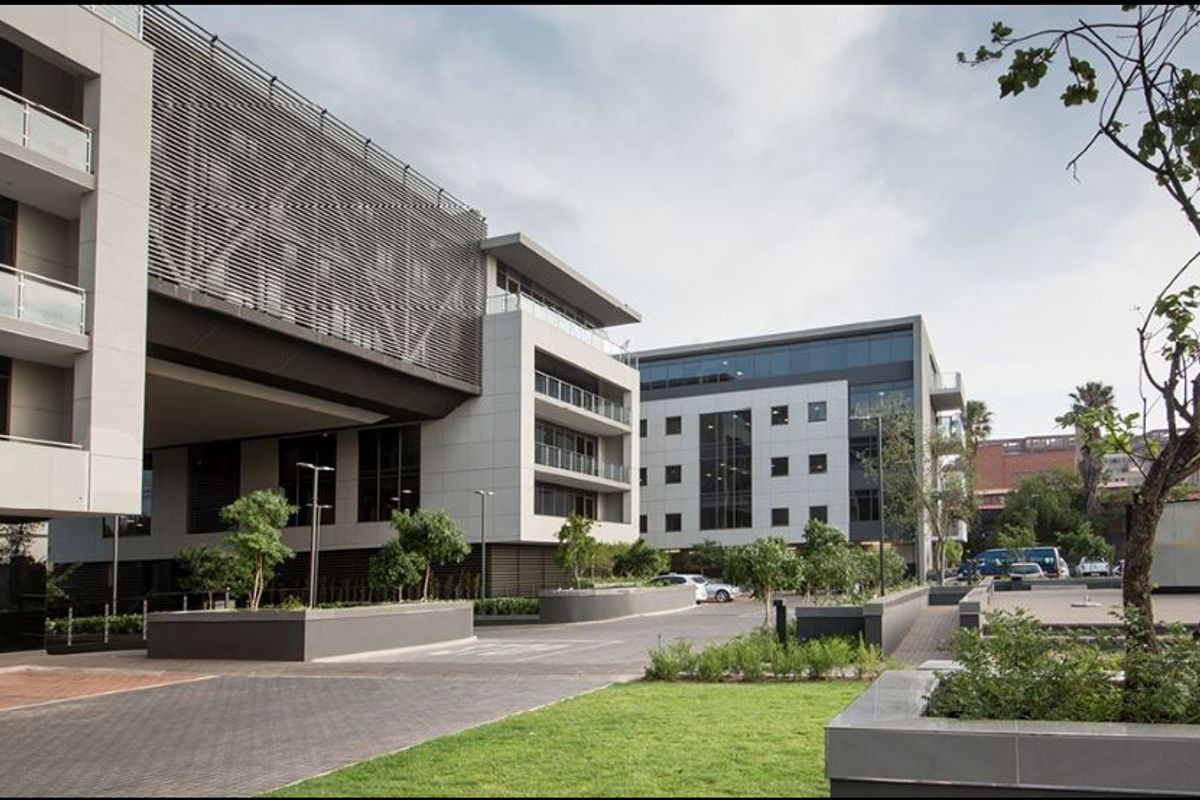 A modern commercial office complex featuring contemporary architectural design, glass balconies, paved driveways, and well-maintained landscaped garden areas.