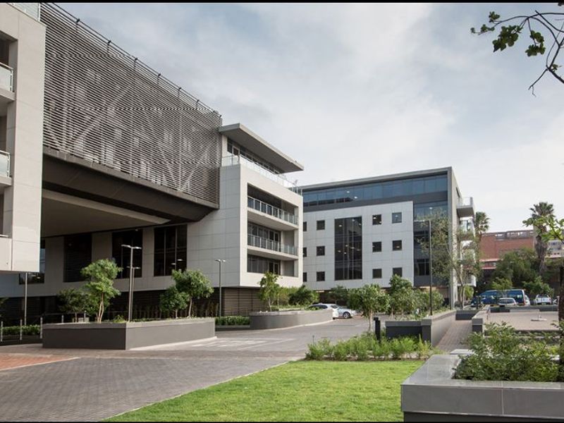 A modern commercial office complex featuring contemporary architectural design, glass balconies, paved driveways, and well-maintained landscaped garden areas.