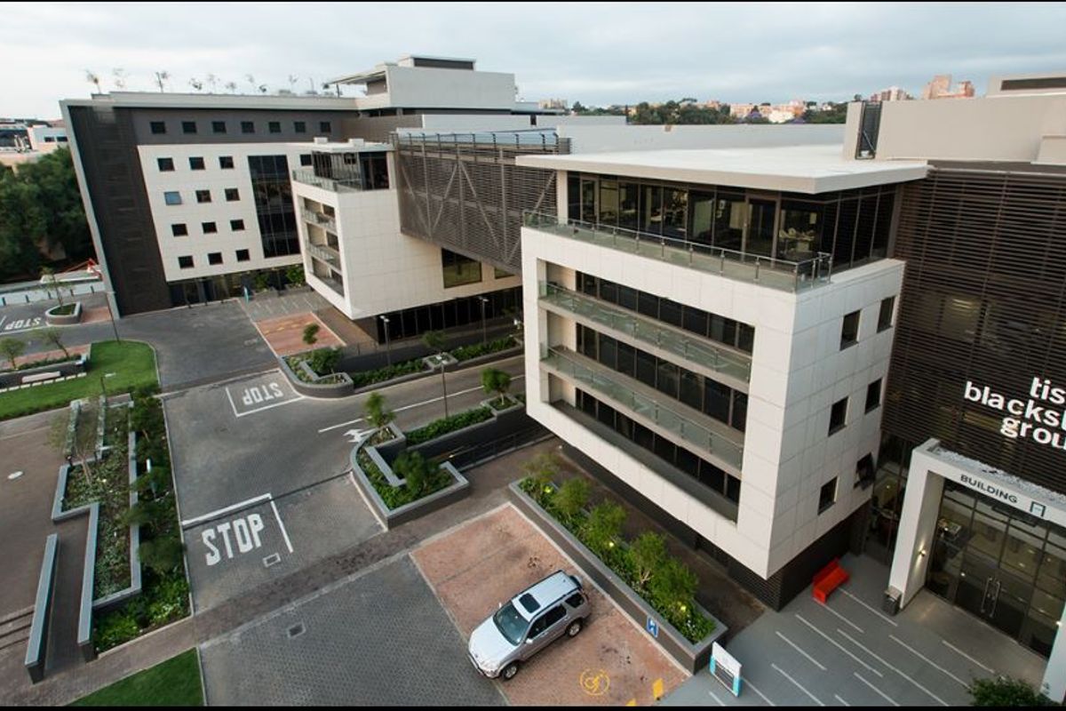 Aerial view of a modern commercial office complex featuring multi-story buildings with glass facades, balconies, and paved parking facilities.