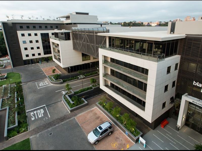 Aerial view of a modern commercial office complex featuring multi-story buildings with glass facades, balconies, and paved parking facilities.