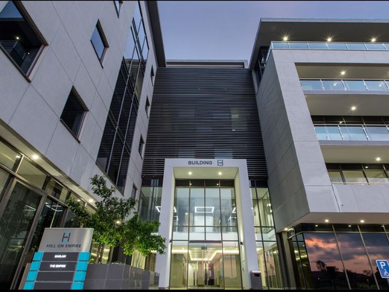 Modern commercial office building facade featuring glass curtain walls, integrated balcony lighting, and a prominent main entrance with professional signage.