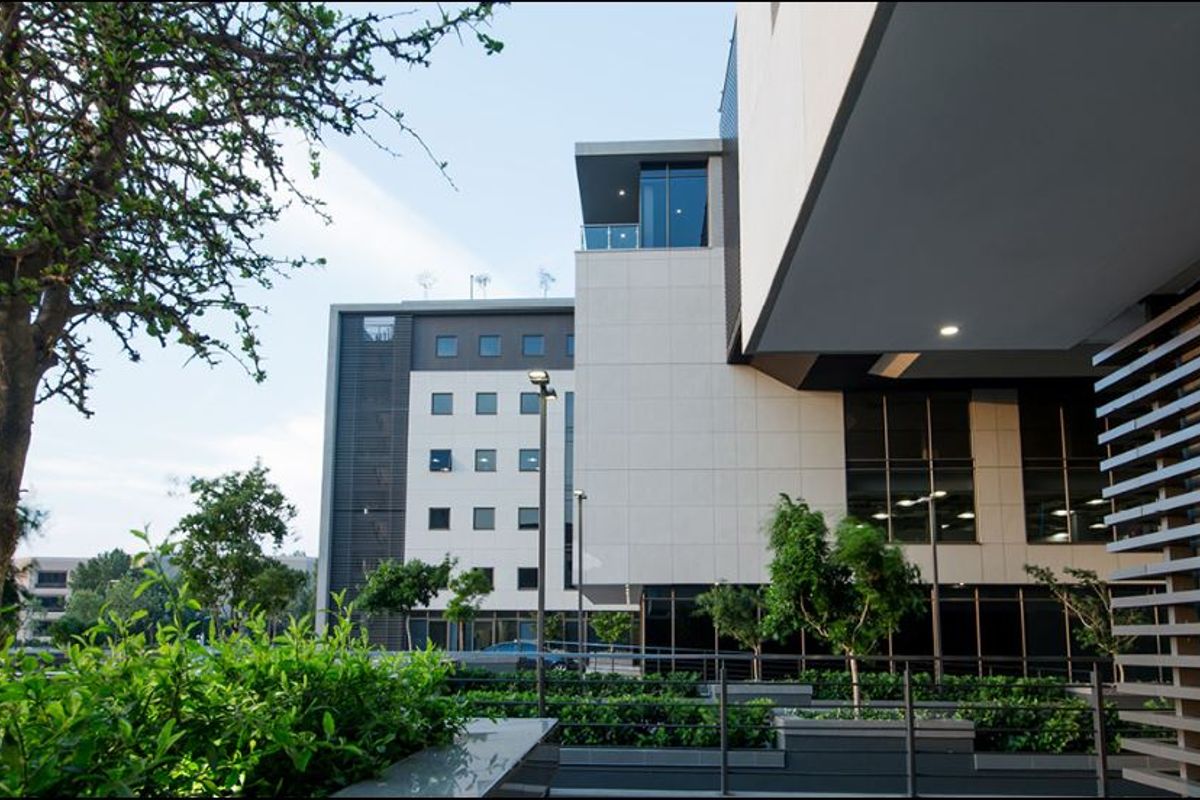 Modern commercial building exterior featuring clean architectural lines, stone cladding, integrated balcony, and landscaped garden planters.