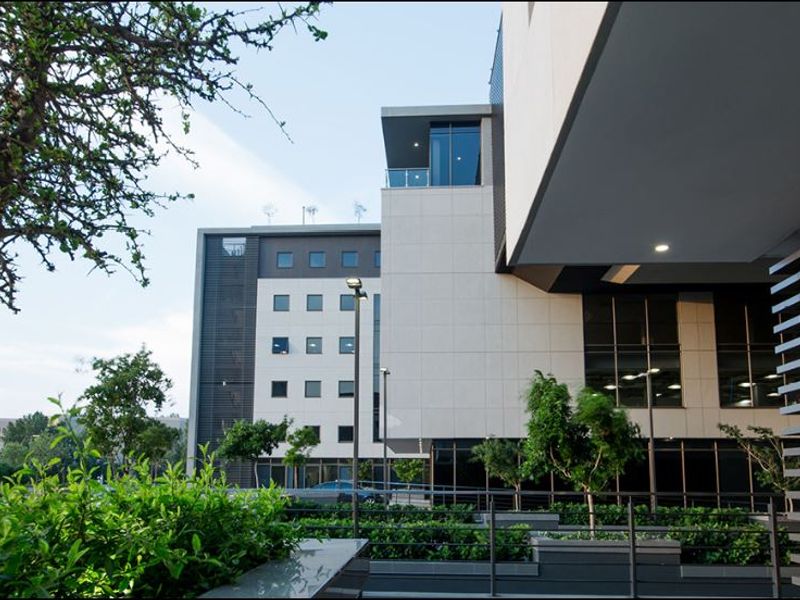 Modern commercial building exterior featuring clean architectural lines, stone cladding, integrated balcony, and landscaped garden planters.