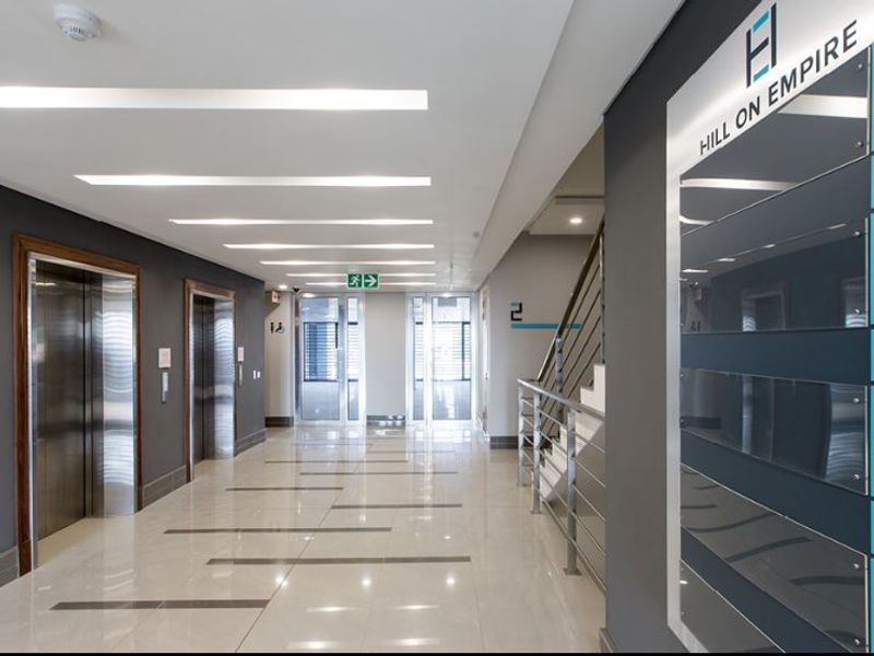Modern commercial building lobby featuring polished tile floors, stainless steel elevator doors, a staircase with metal railings, and clear directory signage.