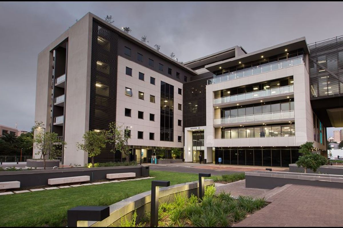 Modern multi-story commercial office building featuring a glass facade, integrated balconies, and well-maintained landscaped grounds with paved walkways.
