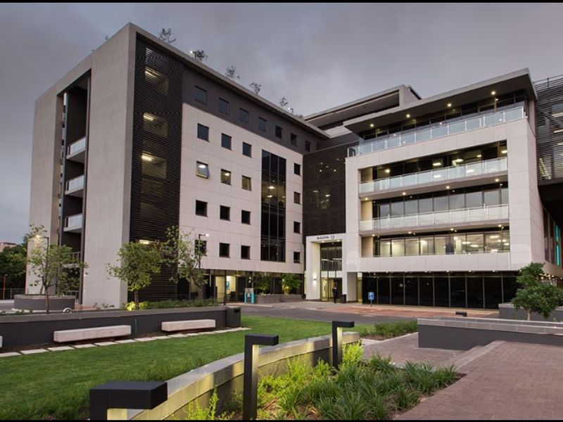 Modern multi-story commercial office building featuring a glass facade, integrated balconies, and well-maintained landscaped grounds with paved walkways.