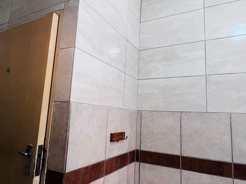 A bathroom corner featuring ceramic wall tiles, a shower tray, and a towel hook, requiring ceiling finishing and door frame repairs.