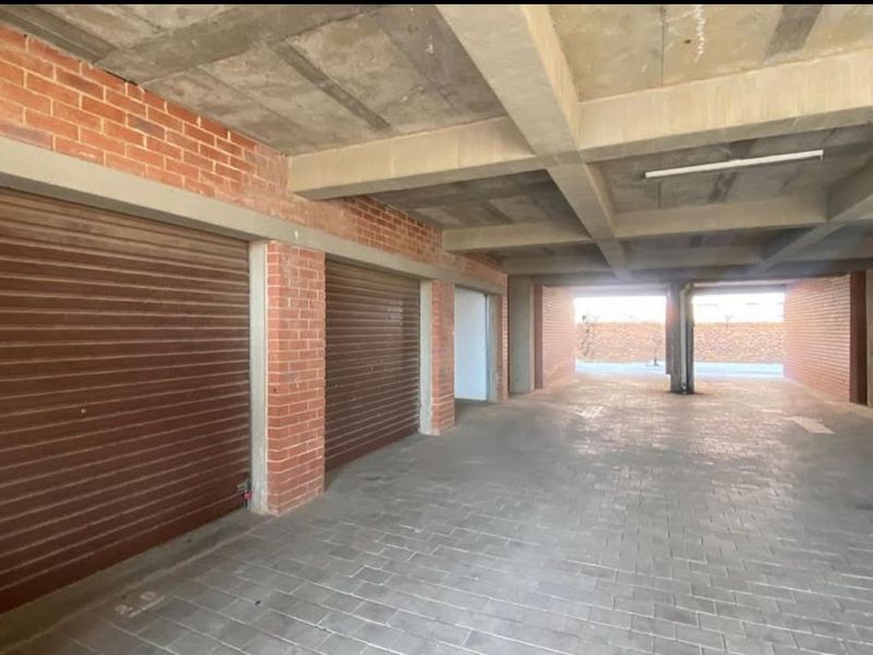 A spacious, covered parking garage featuring exposed concrete ceilings, brick walls, and secure roller shutter doors.