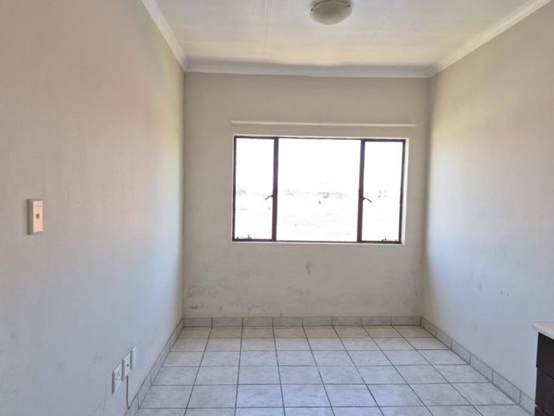 An empty bedroom featuring tiled flooring, neutral walls, and a window, providing a blank canvas ready for personalization.