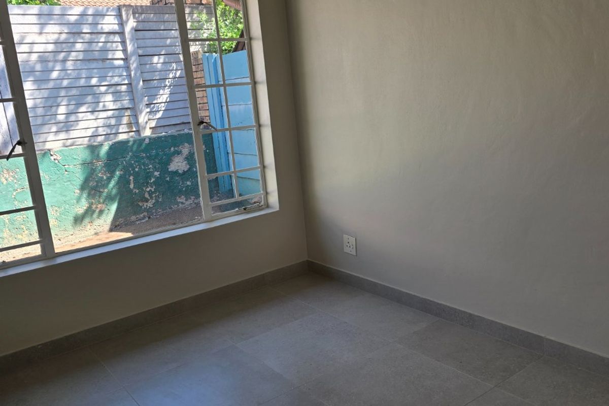 A clean, empty bedroom featuring neutral tiled flooring, a large grid-pattern window, and smooth painted walls, ready for personalization.