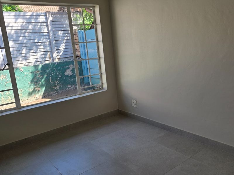 A clean, empty bedroom featuring neutral tiled flooring, a large grid-pattern window, and smooth painted walls, ready for personalization.