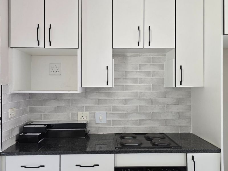 A clean, modern kitchen featuring white cabinetry, dark granite countertops, a subway tile backsplash, and integrated electric oven and hob.