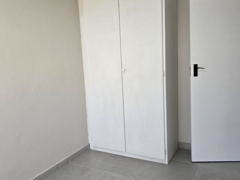 A clean, empty bedroom featuring neutral wall paint, modern grey floor tiles, and a built-in white wardrobe.