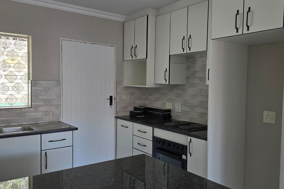 Modern kitchen featuring granite countertops, subway tile backsplash, built-in oven, electric hob, and ample white cabinetry with black hardware.