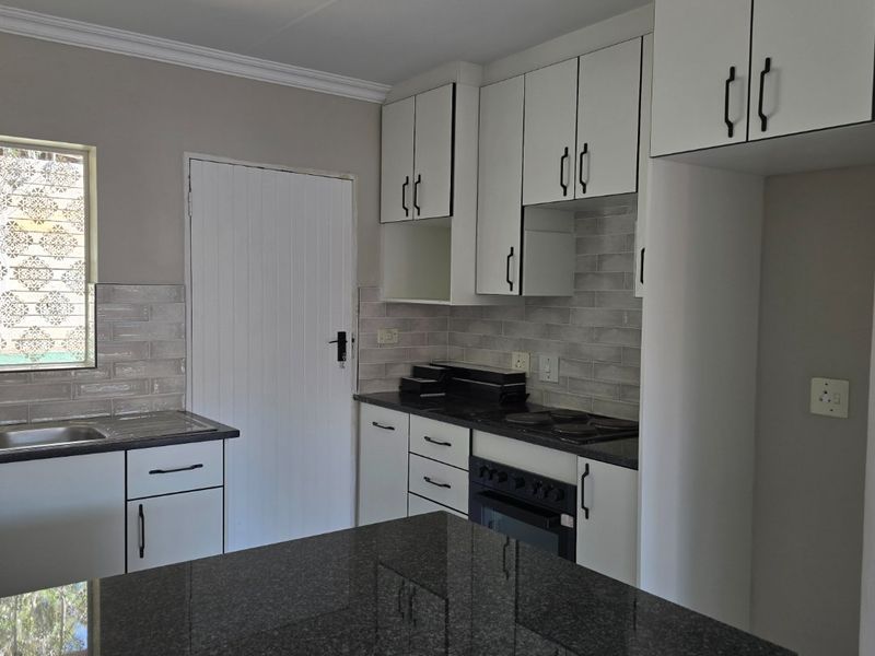 Modern kitchen featuring granite countertops, subway tile backsplash, built-in oven, electric hob, and ample white cabinetry with black hardware.