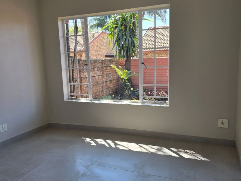 A bright, empty bedroom featuring neutral tiled flooring, coving, and a large window overlooking the rear garden area.