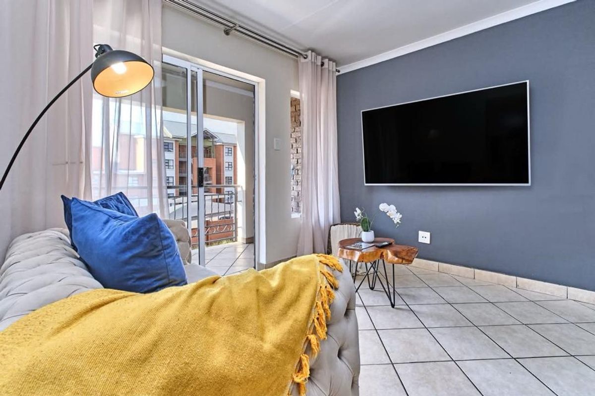 A well-lit living room featuring tiled flooring, a dark grey accent wall, and a sliding glass door providing access to a balcony.