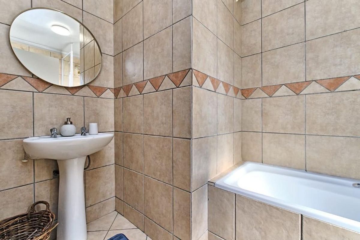 A functional bathroom featuring a pedestal basin, built-in bathtub, and full-height ceramic wall tiling with a decorative border.