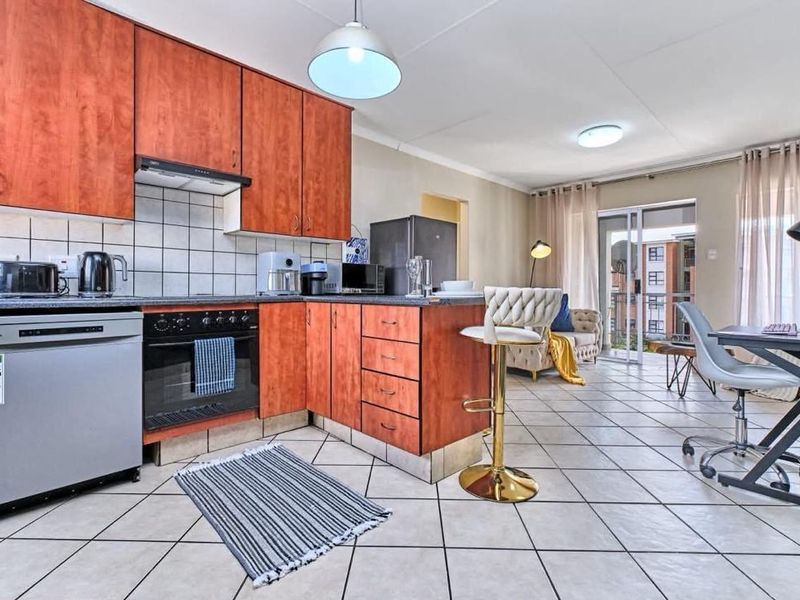 Open-plan kitchen and living area featuring wood-finish cabinetry, tiled flooring, and direct access to a balcony through sliding glass doors.