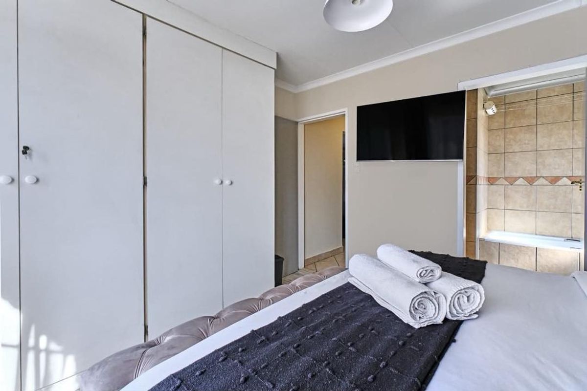 Bedroom featuring built-in cupboards and an adjoining en-suite bathroom with tiled finishes.