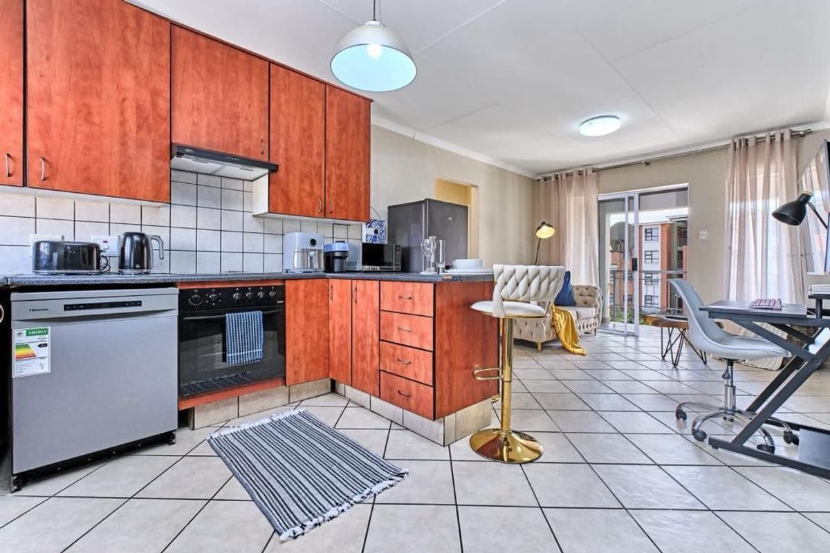 Open-plan kitchen and living area featuring wood-finish cabinetry, tiled flooring, and direct access to a balcony through sliding glass doors.