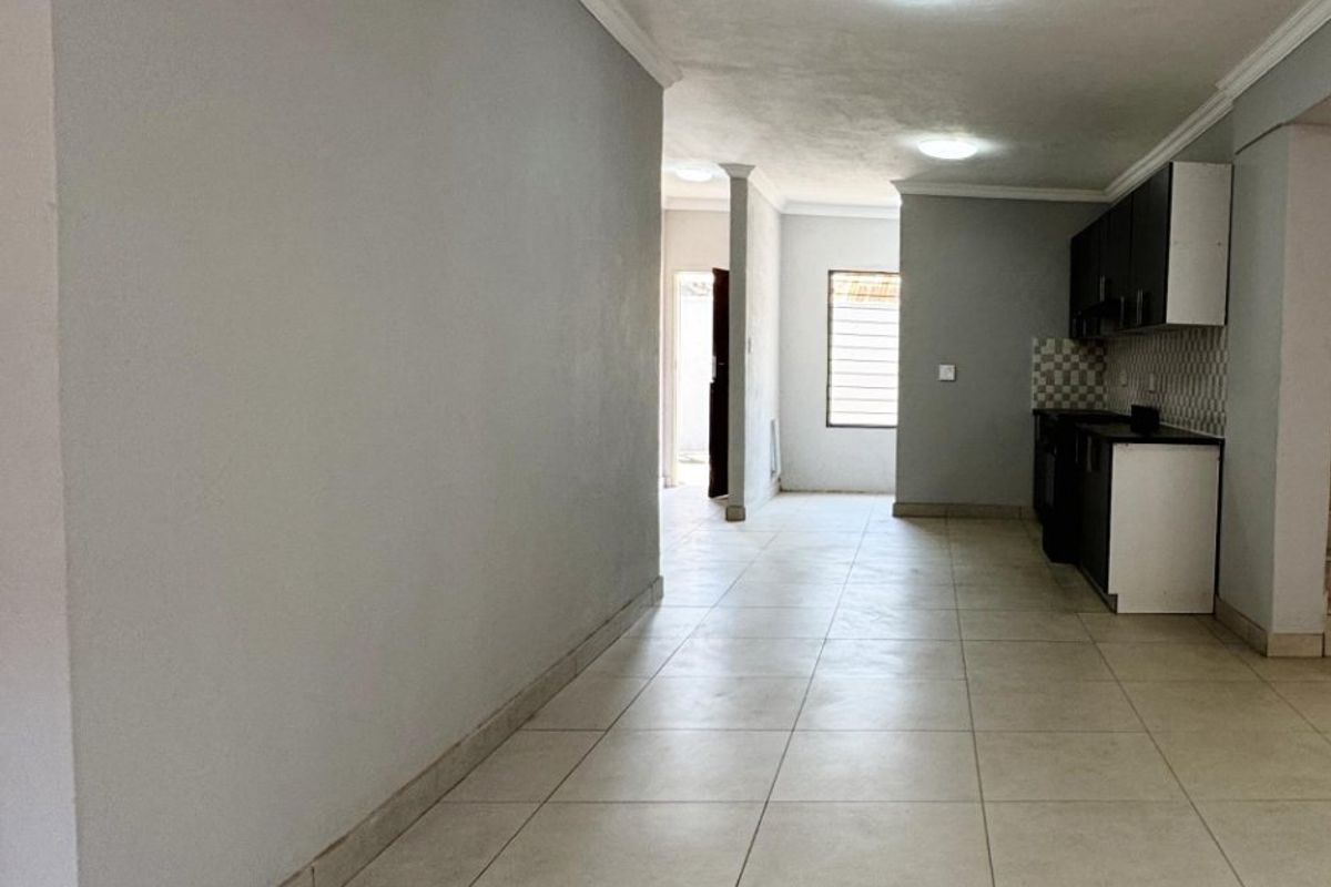 Spacious open-plan living area featuring neutral tiled flooring, coved ceiling cornices, and a functional kitchen with built-in cabinetry and a tiled backsplash.