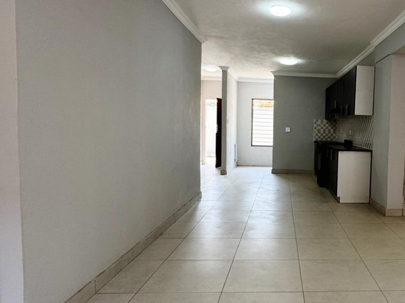 Spacious open-plan living area featuring neutral tiled flooring, coved ceiling cornices, and a functional kitchen with built-in cabinetry and a tiled backsplash.