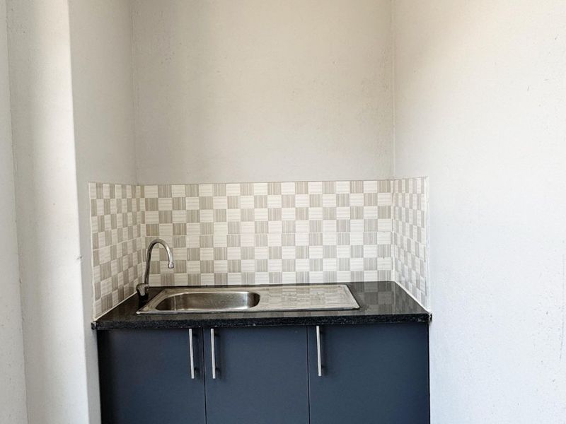 A compact laundry or utility area featuring dark grey cabinetry, a stainless steel sink, and a decorative checkered tile backsplash.