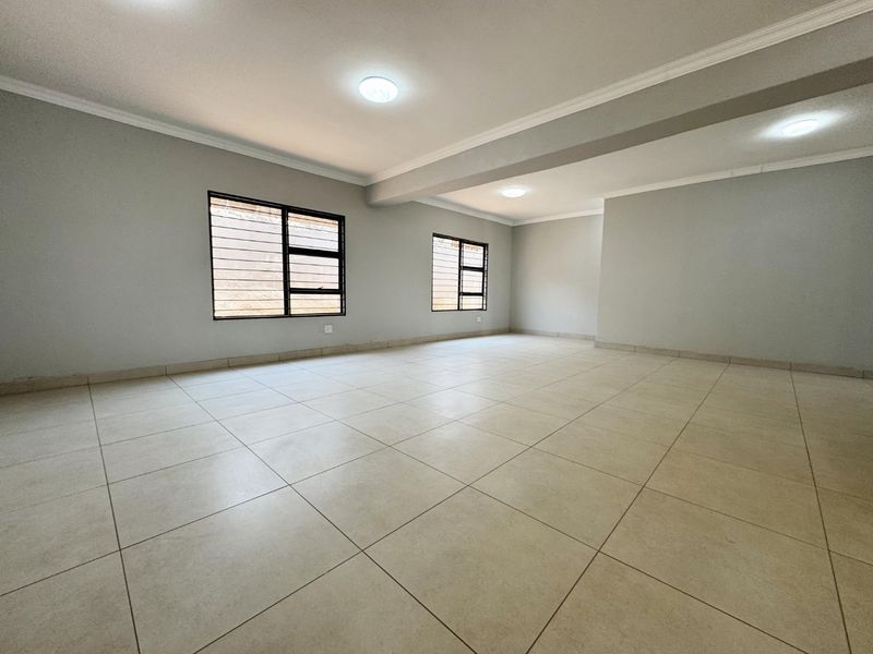 A spacious, empty living area featuring neutral tiled flooring, clean walls, and security-fitted windows, providing a versatile blank canvas for interior design.