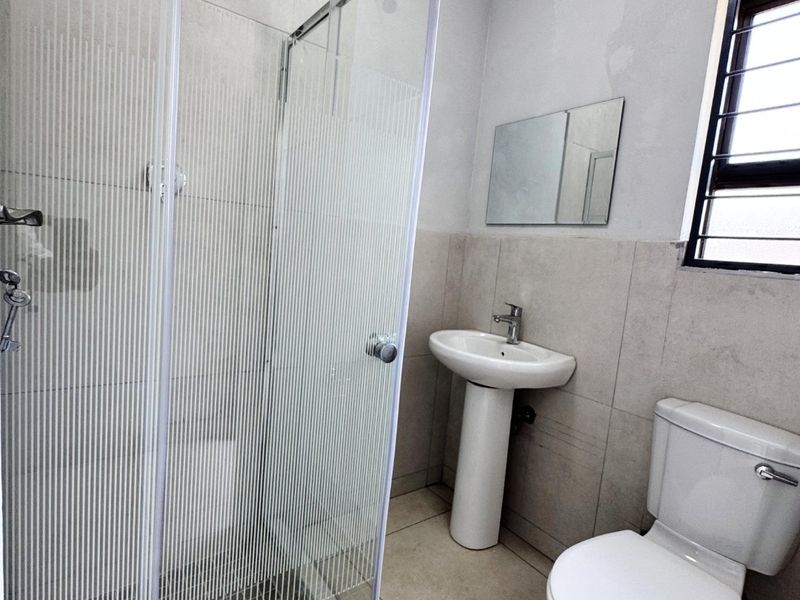A functional bathroom featuring a glass shower enclosure, pedestal basin, toilet, and neutral wall and floor tiling.
