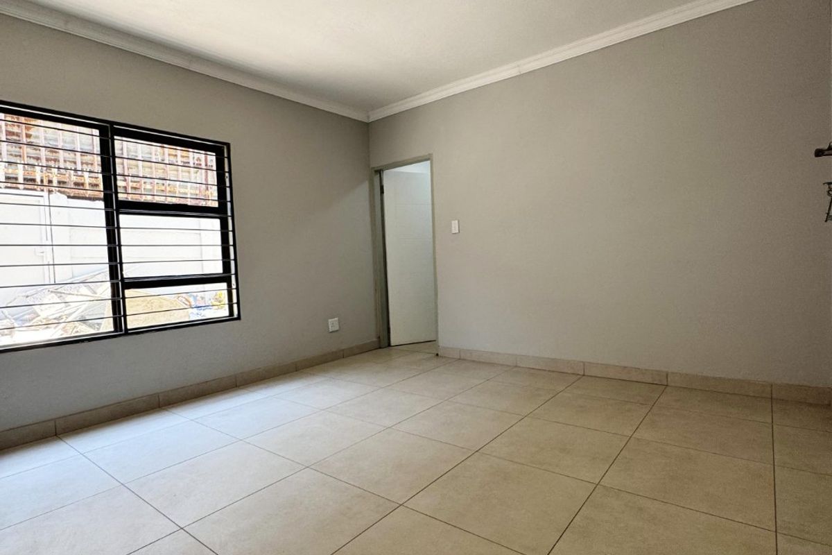 An empty bedroom featuring neutral tiled flooring, security bars on the window, and cove cornicing, currently awaiting a new light fixture.