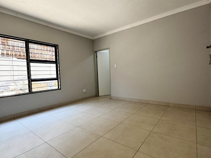 An empty bedroom featuring neutral tiled flooring, security bars on the window, and cove cornicing, currently awaiting a new light fixture.
