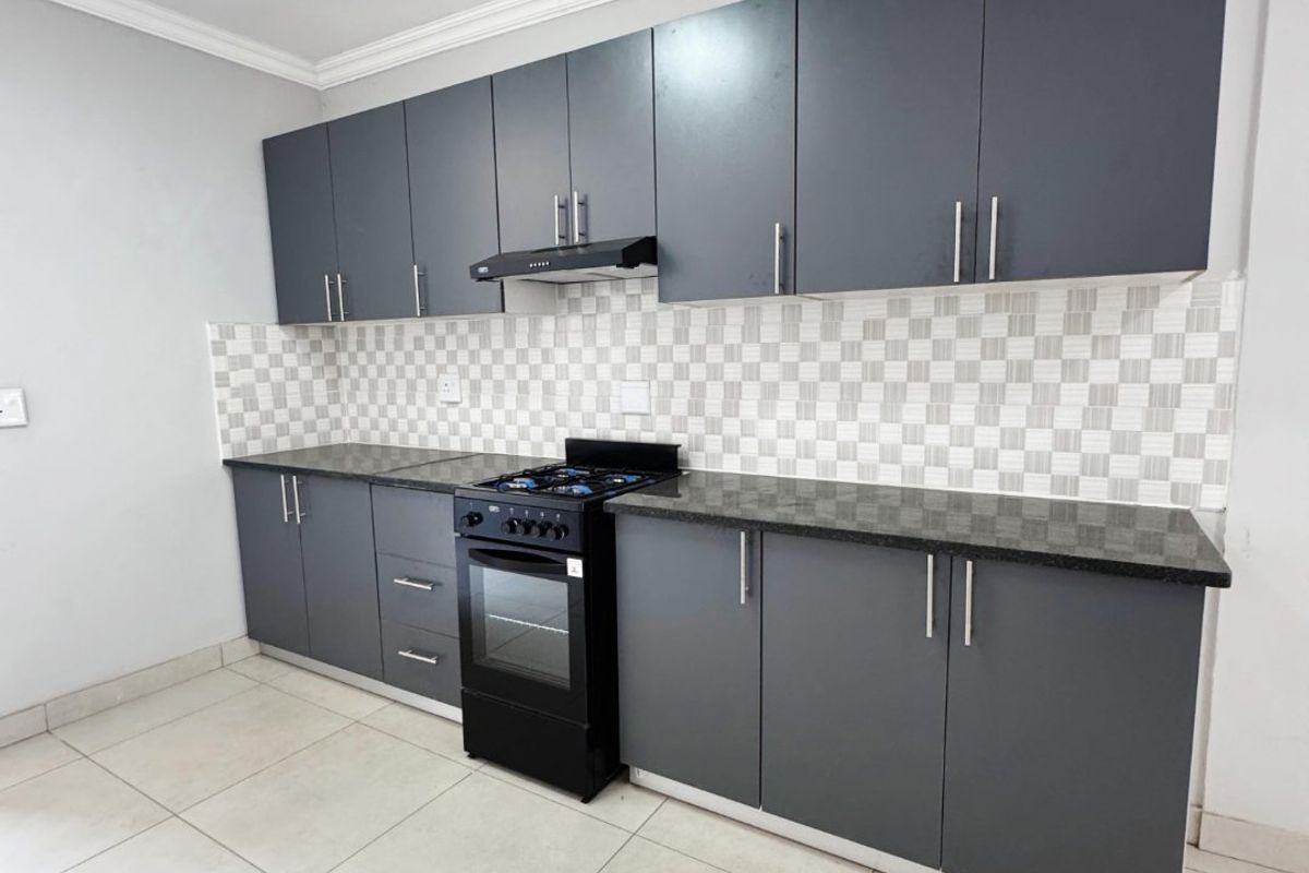 A modern, clean kitchen featuring dark grey cabinetry, granite countertops, a mosaic tile backsplash, and a built-in oven with a gas hob.