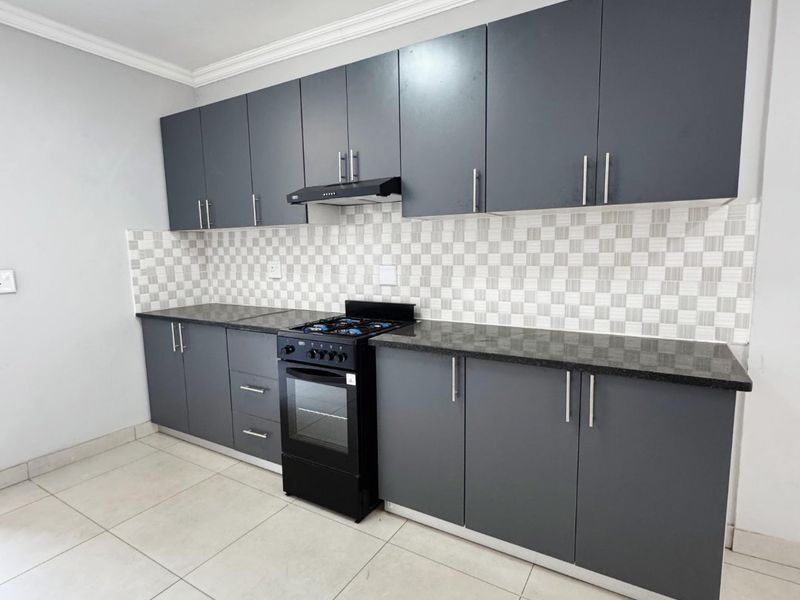 A modern, clean kitchen featuring dark grey cabinetry, granite countertops, a mosaic tile backsplash, and a built-in oven with a gas hob.