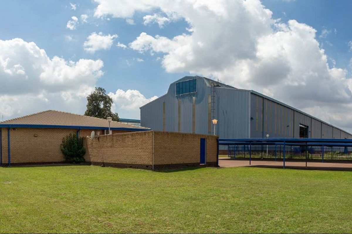 Exterior view of an industrial property featuring a brick building section and a large metal-clad warehouse structure with a covered walkway.