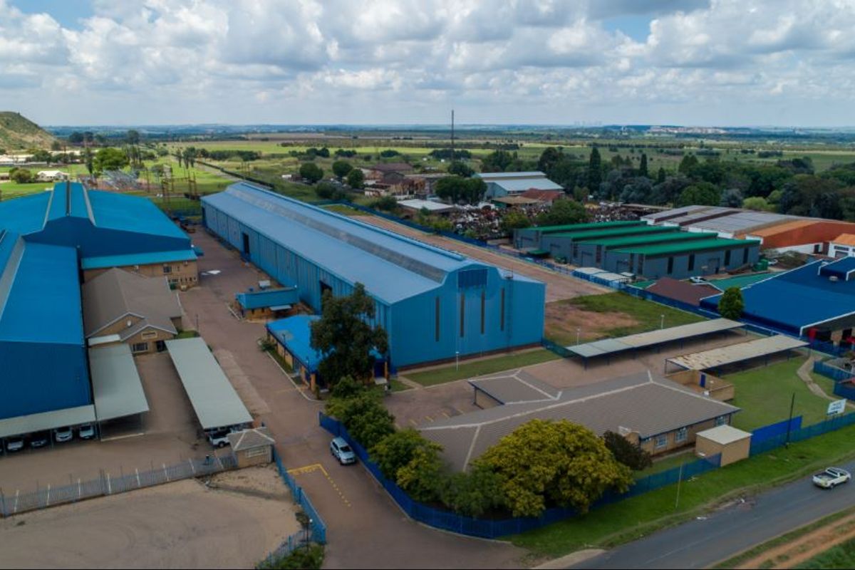 Aerial view of a large industrial facility featuring multiple warehouse structures, extensive paved yard space, covered parking, and secure perimeter fencing.