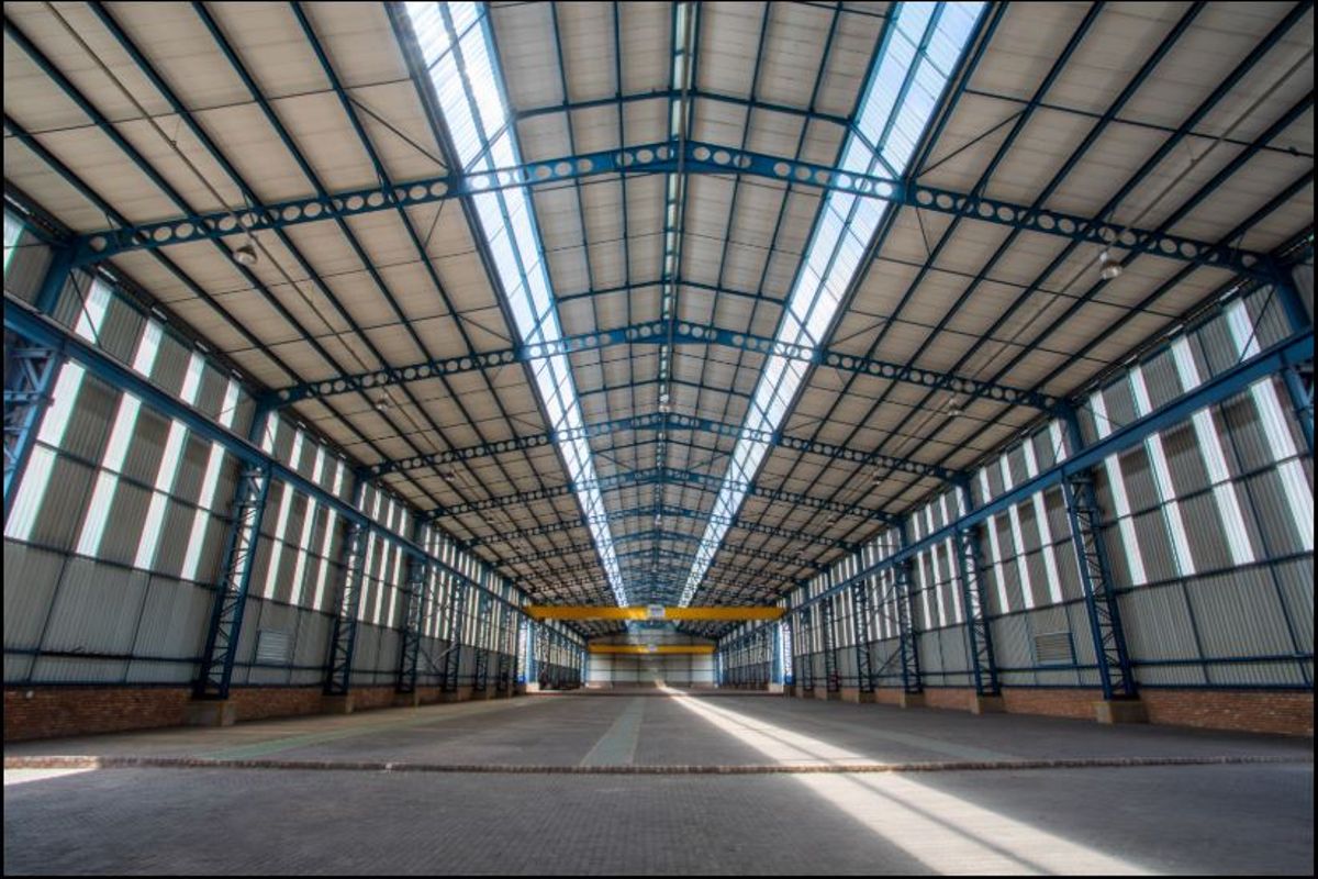 Spacious industrial warehouse featuring a high-clearance steel truss roof, integrated skylights, and an overhead crane beam, providing an expansive open-plan floor area.