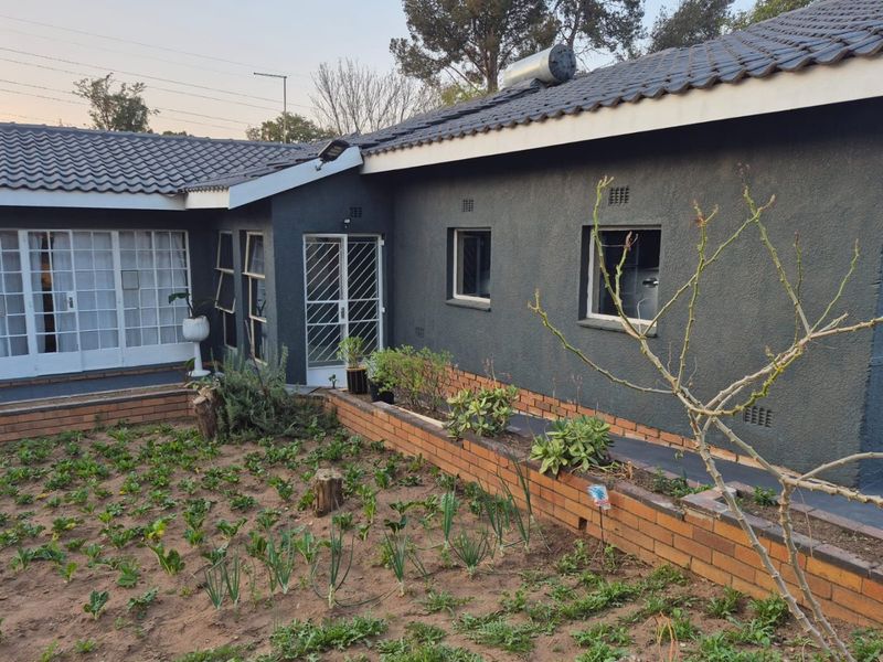 Rear view of the house featuring a dark grey textured facade, tiled roof with solar geyser, and a brick planter box in the garden.