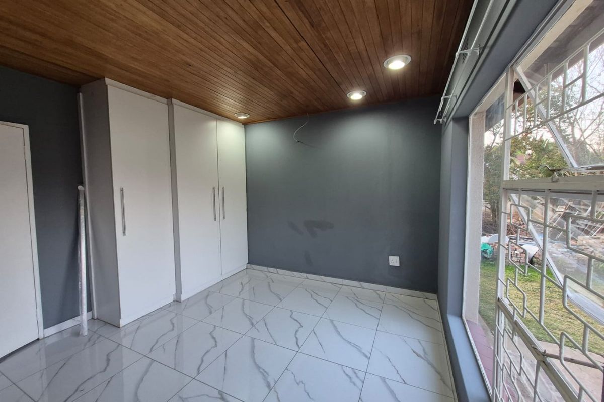A bright, empty bedroom featuring modern marble-look floor tiles, built-in cupboards, and a warm timber-paneled ceiling with recessed lighting.