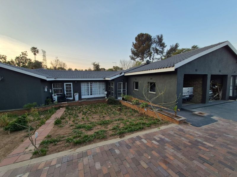 Front exterior view of a single-story house featuring a double garage, brick paved driveway, and a landscaped garden area with a solar geyser.