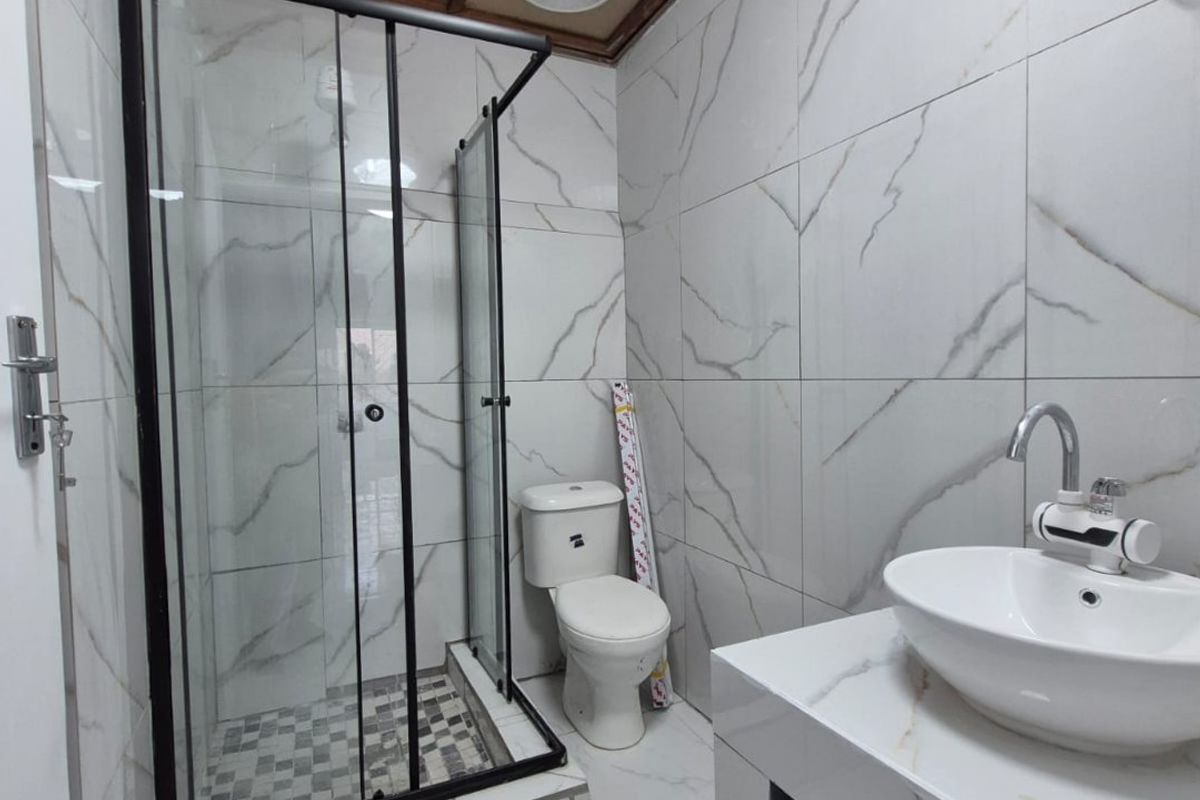 Modern bathroom featuring marble-look tiled walls and floors, a glass-enclosed shower, vessel sink, and a warm timber-paneled ceiling.